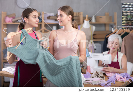 Dressmaker talks to a woman and shows a dress 128435559