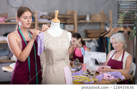Mature head of manufacturing and female assistant sewing, young designer work with mannequin. 128435636
