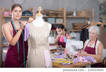 Mature head of manufacturing and female assistant sewing, young designer work with mannequin. 128435644