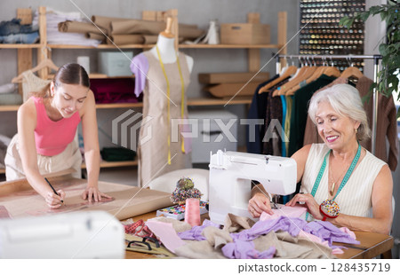 Elderly woman sewing female assistant drawing pattern on paper 128435719