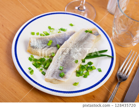 On wooden table is plate with appetizer - salted Atlantic herring fillet with pickled onions On wooden table is plate with appetizer - salted Atlantic herring fillet with pickled onions 128435720