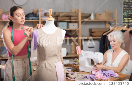 Senior woman tailor busy with sewing machine, female employee work with mannequin Senior woman tailor busy with sewing machine, female employee work with mannequin 128435740
