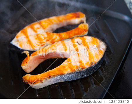 There are two pieces of broiled salmon steaks in square black frying pan 128435840