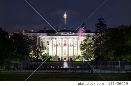 Illuminated night view of the White House in Washington, D.C., with the American flag flying beside the iconic neoclassical structure, symbolizing national leadership and heritage 128436059
