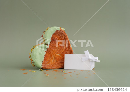 Empty paper note template mock up. Heart shaped pistachio croissant on green background with copy space. Puff pastry trendy sweet dessert bakery. Creamy dough experiment  128436614