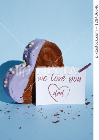 WE LOVE YOU DAD caption on paper greeting holiday card Father's Day Heart shaped blueberry flavor croissant on blue background with copy space. Puff pastry new trendy sweet dessert bakery. Creamy 128436646