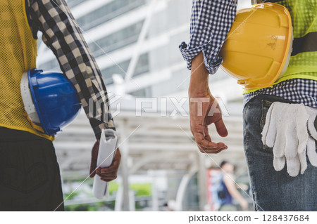 Helmet construction Engineer team. Men hands holding hardhat yellow work helmet in Civil Construction Engineering. Close up engineer man hold safety yellow worker helmet hard hat at Construction Site 128437684
