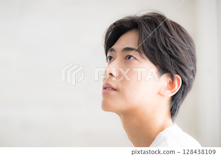 A man with a clear complexion touching his black hair. Close-up image of hair care. Serious and serious expression. 128438109