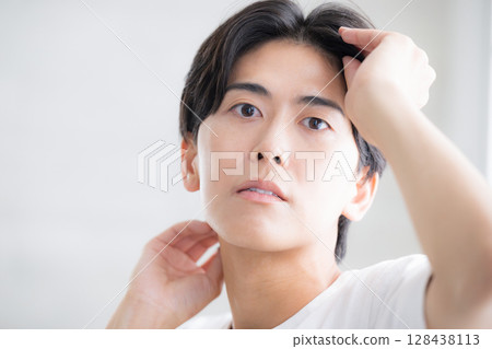 A man with a clear complexion touching his black hair. Close-up image of hair care. Serious and serious expression. 128438113
