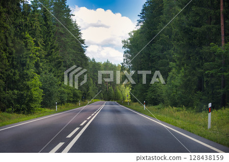 Peaceful Country Road Surrounded by Dense Green Forest under Blue Skies 128438159