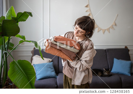 Young woman calmly sorting freshly washed bedding clothes at home. Laundry routine, textile care Young woman calmly sorting freshly washed bedding clothes at home. Laundry routine, textile care 128438165