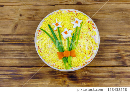 Traditional russian layered salad Mimosa with spring decoration Daffodil on wooden table. Top view. Decoration is made of egg, green onion and carrot Traditional russian layered salad Mimosa with spring decoration Daffodil on wooden table. Top view. Decoration is made of egg, green onion and carrot 128438258
