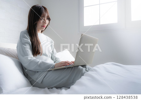 一位女士在床上低頭使用電腦。生活方式、自由工作、工作風格和忙碌工作的圖片。 128438538