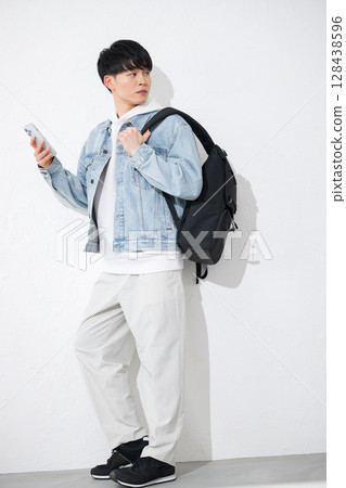 一位 20 多歲的年輕男子手持智慧型手機，微笑著敲擊螢幕。全身白色背景 128438596