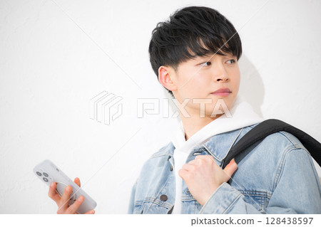 A young man in his 20s holding a smartphone and tapping with a smile on a white background 128438597