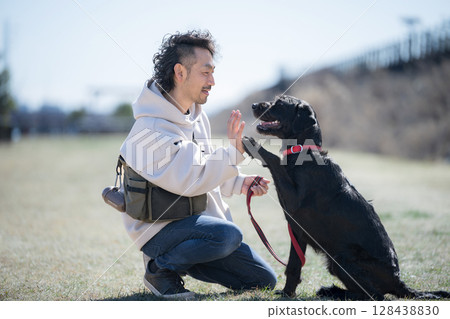 A man and his dog enjoying a walk on a riverbank under the blue sky. They look at each other, give each other high fives, and shake hands. An image of trust, best friends and buddies. 128438830