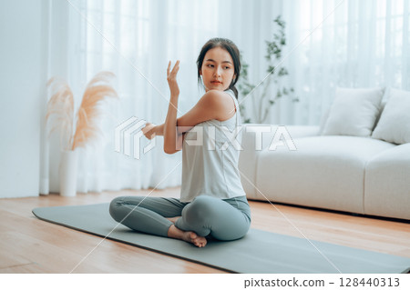 Happy young Asian woman practicing yoga and shoulder stretching at home 128440313