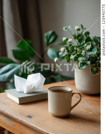 A serene workspace features a cup of tea, a tissue box, and a vibrant indoor plant on a desk, creating a cozy atmosphere for relaxation and productivity. 128440778