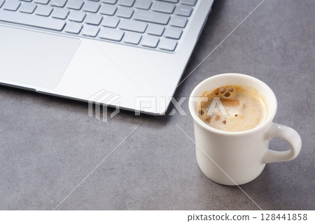 坐在辦公桌前用筆記型電腦工作,同時喝著現煮的美味咖啡的圖片 坐在辦公桌前用筆記型電腦工作,同時喝著現煮的美味咖啡的圖片 128441858