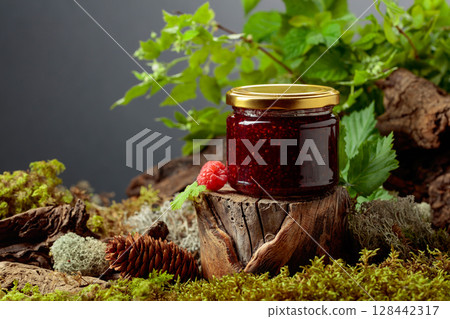 A jar of raspberry jam with fresh berries on an old tree trunk in the forest. A jar of raspberry jam with fresh berries on an old tree trunk in the forest. 128442317