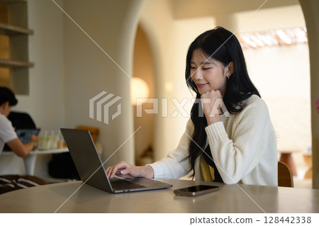Relaxed freelancer working on a laptop at a cozy cafe 128442338