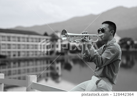 Black and white image of trumpet player performing near a tranquil lake with mountains in the background Black and white image of trumpet player performing near a tranquil lake with mountains in the background 128442364