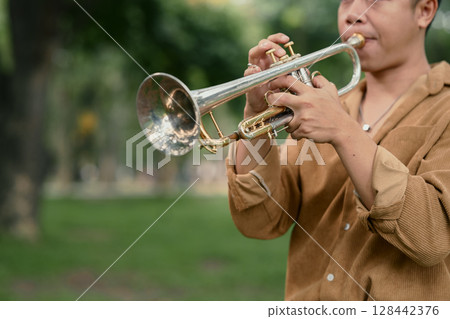 Young man playing trumpet in a park, enjoying music in a peaceful outdoor 128442376