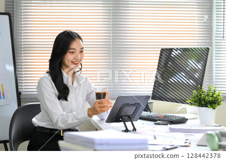 Smiling businesswoman analyzing financial data on a digital tablet in a modern office 128442378
