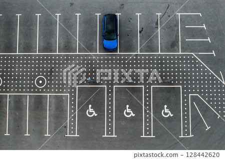 The blue car is parked in a parking lot and there are places for the disabled 128442620