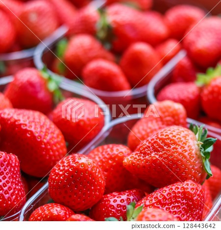 Fresh, vibrant red strawberries are neatly packed in clear plastic containers, highlighting their juicy appeal and readiness for sale or consumption. High quality photo 128443642