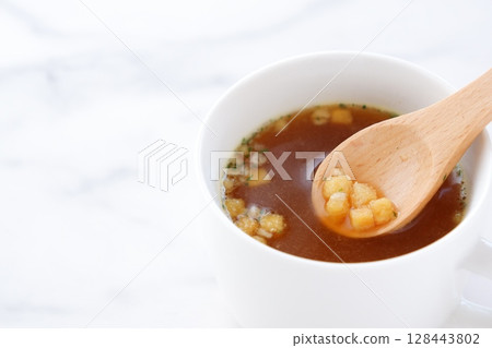 Stir the hot onion consommé soup with a wooden spoon Stir the hot onion consommé soup with a wooden spoon 128443802