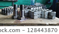 Close-up of new metal bolts and nuts. Steel bolts and nuts. Industrial fasteners displayed on a wooden surface, with a blurred workshop background. Flanged steel hex nuts. Mechanical engineering. 128443870