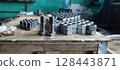 Steel bolts and nuts. Industrial fasteners displayed on a wooden surface, with a blurred workshop background. Flanged steel hex nuts. Close-up of new metal bolts and nuts. Mechanical engineering. 128443871