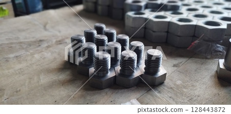 Close-up of a set of new metal bolts. Hex head bolts in focus, with nuts in the background. Industrial fasteners on a wooden surface. Selective focus with blurred background. Close-up of a set of new metal bolts. Hex head bolts in focus, with nuts in the background. Industrial fasteners on a wooden surface. Selective focus with blurred background. 128443872