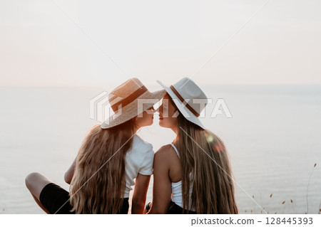 Two Young Women in Straw Hats Face Each Other by the Sea Two Young Women in Straw Hats Face Each Other by the Sea 128445393