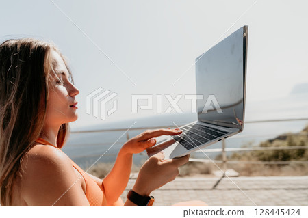 Woman Using Laptop on a Sunny Day by the Sea 128445424