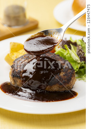 A scene where sauce is poured onto a hamburger steak served on a dinner plate 128447475