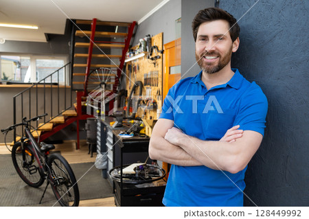 Man bike mechanic standing workshop entrance wearing blue t-shirt Man bike mechanic standing workshop entrance wearing blue t-shirt 128449992