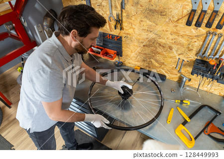Skilled bike mechanic man using tools repairing bicycle in well-organized workshop Skilled bike mechanic man using tools repairing bicycle in well-organized workshop 128449993