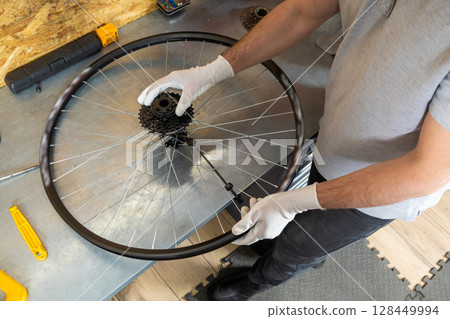 Mechanic man servicing bike using specialized tools in busy workshop 128449994
