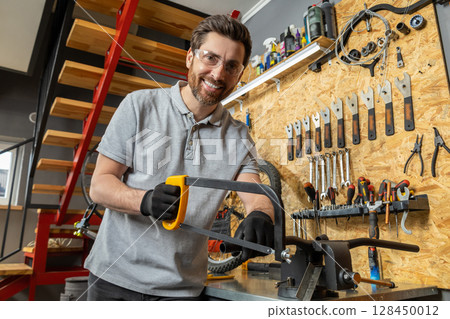 Velomechanic in professional attire servicing bicycle with specialized tools in workshop setting 128450012