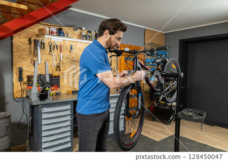 Bearded mechanic working on bike frame in workshop for cycle repair 128450047