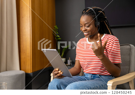 Cute african american young woman in headphones with a tablet in hands 128450245