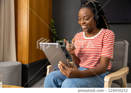 Cute african american young woman in headphones with a tablet in hands Cute african american young woman in headphones with a tablet in hands 128450252