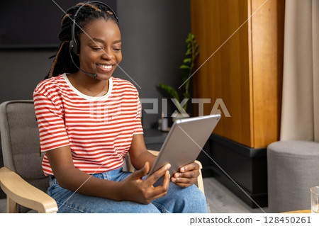 Cute african american young woman in headphones with a tablet in hands 128450261