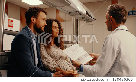 Photo of a couple sitting in a fertility clinic, holding hands tightly, doctor showing them medical documents Photo of a couple sitting in a fertility clinic, holding hands tightly, doctor showing them medical documents 128450306