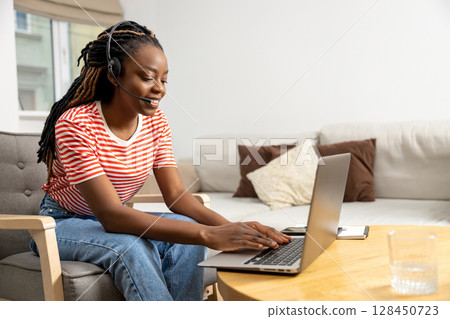 Smiling cute long-haired african american young woman working online Smiling cute long-haired african american young woman working online 128450723