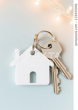 House shaped keychain with keys lying on soft blue backdrop, bathed in warm fairy lights, symbolizing home comfort and fresh life chapter 128450946