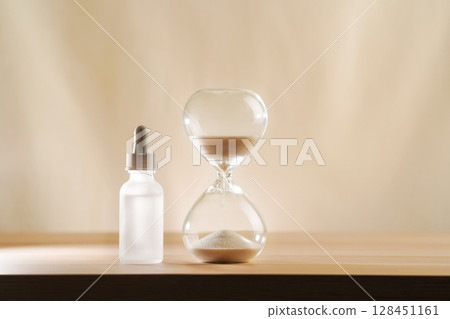 A modern still life featuring skincare product with an hourglass, embodying timeless beauty and minimalism. A focus on creativity and elegance in self-care displayed on a serene, neutral backdrop. 128451161