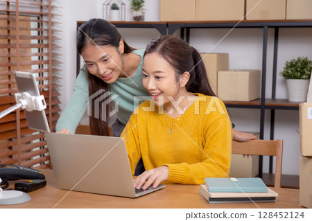 Two young asian woman working on laptop while managing and planning online business. Two young asian woman working on laptop while managing and planning online business. 128452124